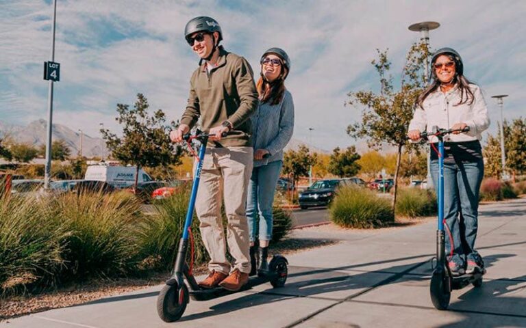 Jóvenes montados sobre patinetes eléctricos en la acera.